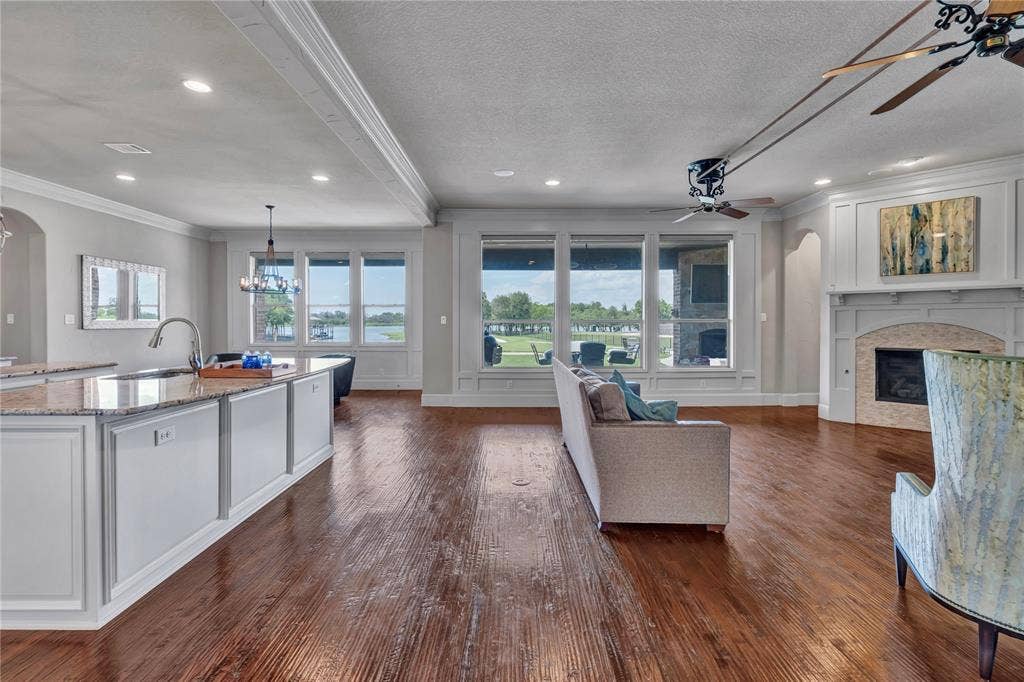 6412 Preferred Drive, Fort Worth, TX 76179 Open-concept living area with wood-finish flooring, a kitchen island with stone countertops and a sink, extensive window views, recessed lighting, and a fireplace with a decorative mantel and hearth