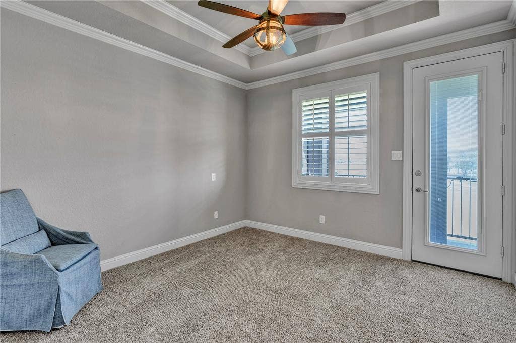 6412 Preferred Drive, Fort Worth, TX 76179 Carpeted room featuring a tray ceiling, ceiling fan with light fixture, white plantation shutters, and a glass-paneled door opening to a balcony with black metal railings