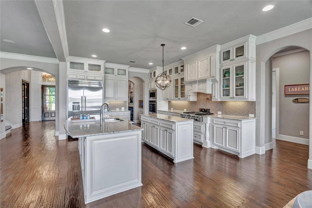 6412 Preferred Drive, Fort Worth, TX 76179 Gourmet kitchen featuring a large central island with an undermount sink, granite countertops, stainless steel appliances, and abundant white cabinetry with glass-front accents