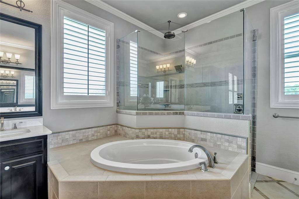 6412 Preferred Drive, Fort Worth, TX 76179 Spa-like bathroom featuring a built-in soaking tub, a glass-enclosed shower with a rainfall showerhead, and a vanity with a white countertop and dark cabinetry