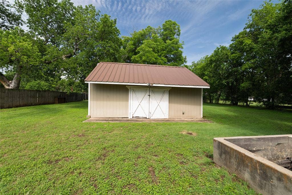 313 N Roe Street, White Settlement, TX 76108 Storage shed featuring a brown metal roof, light tan siding, and white double doors with crossbuck detailing