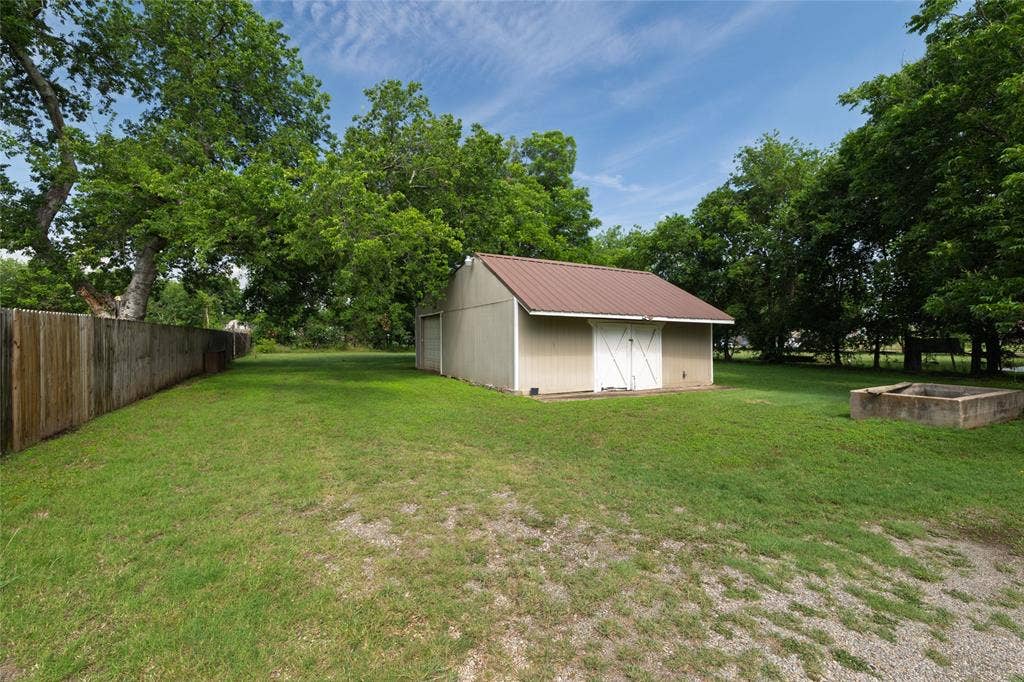 313 N Roe Street, White Settlement, TX 76108 Expansive yard featuring a detached storage building with a metal roof and double barn doors, a wooden privacy fence, mature trees, and a concrete planter box