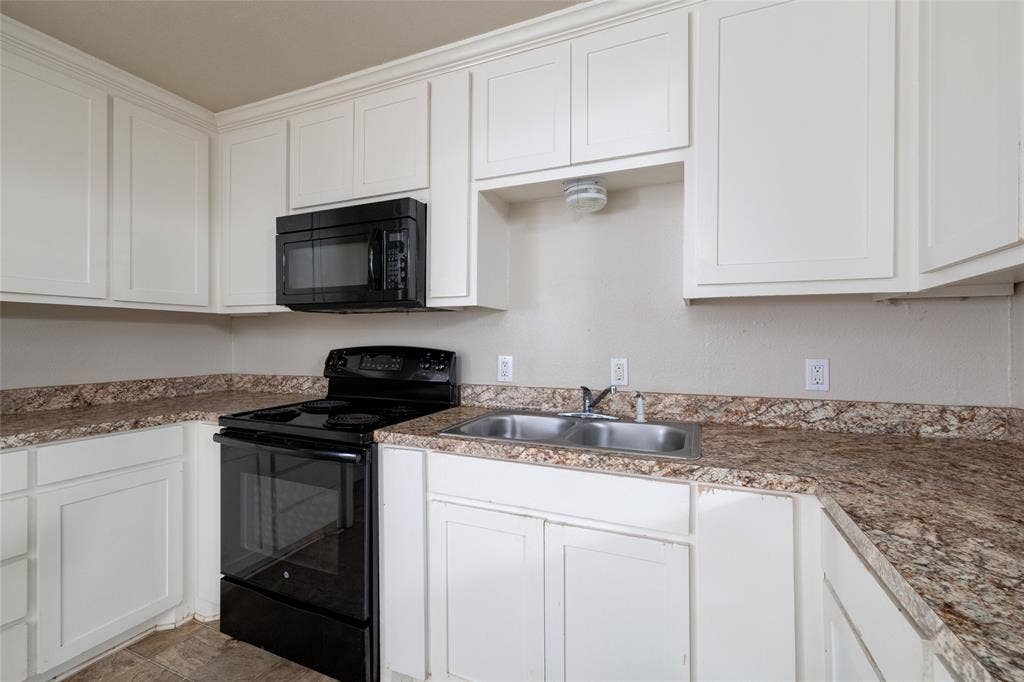 313 N Roe Street, White Settlement, TX 76108 Kitchen featuring white cabinetry with crown molding, black freestanding range, coordinating black over-the-range microwave, double basin stainless steel sink, and speckled countertops