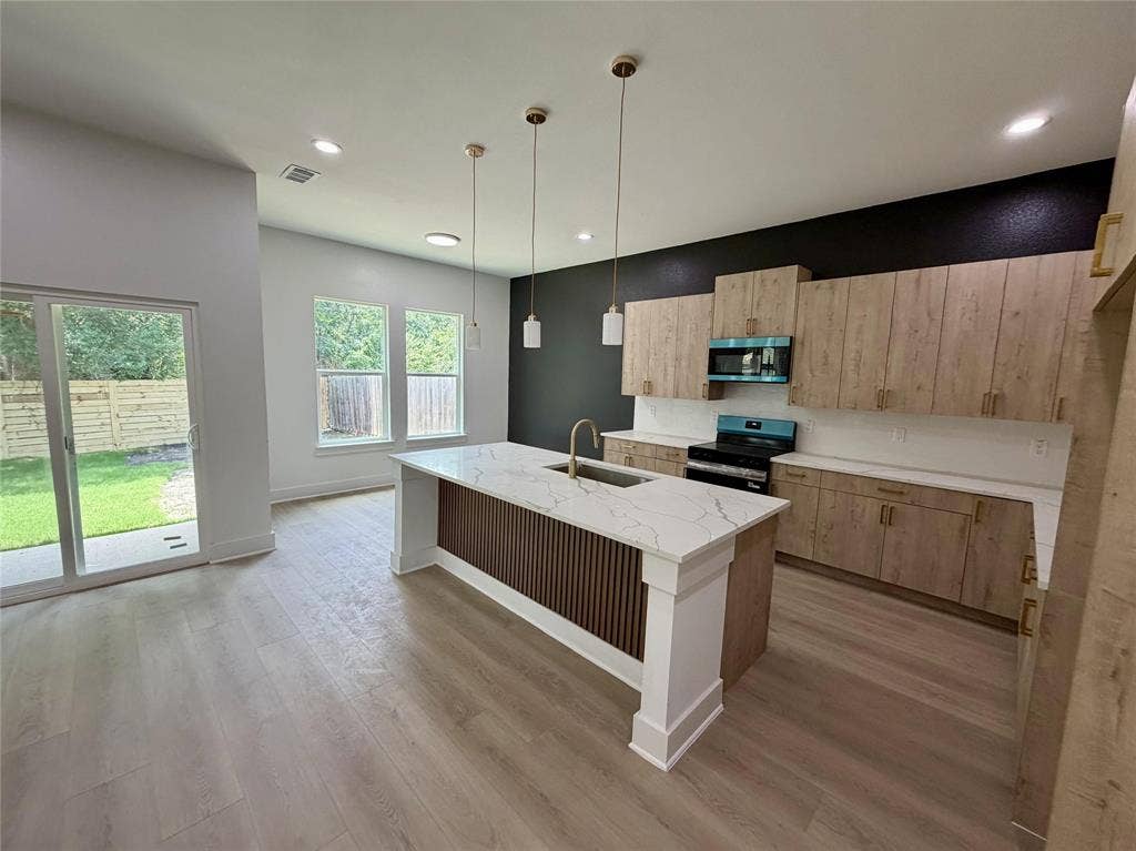 2823 Curvilinear Court, Dallas, TX 75227 Open-concept kitchen featuring an island with a white countertop and integrated sink, light wood-finish cabinetry, and a black wall accent