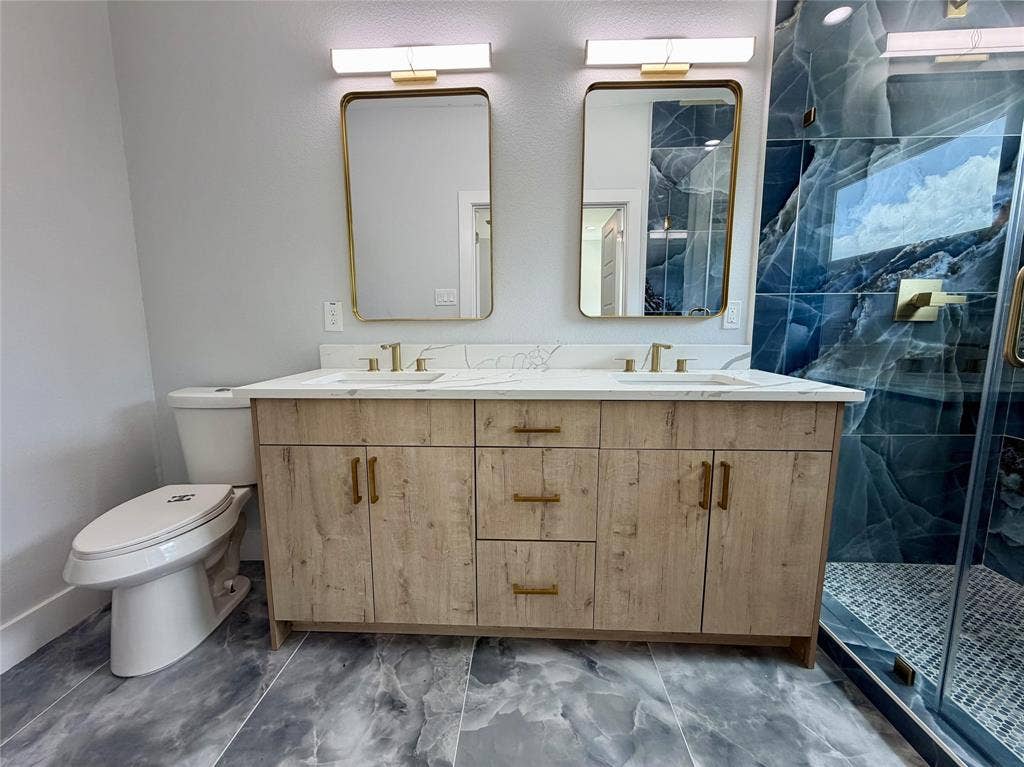 2823 Curvilinear Court, Dallas, TX 75227 Double vanity featuring a wood-finish cabinet with gold-toned hardware, dual rectangular mirrors with gold frames, and white countertops