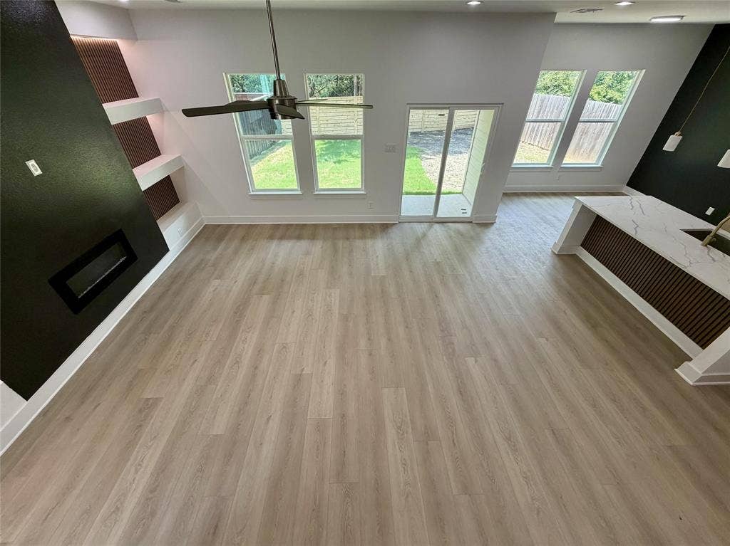 2823 Curvilinear Court, Dallas, TX 75227 Spacious open-concept living area featuring light wood-finish flooring, a modern fireplace with a black surround, and built-in shelving