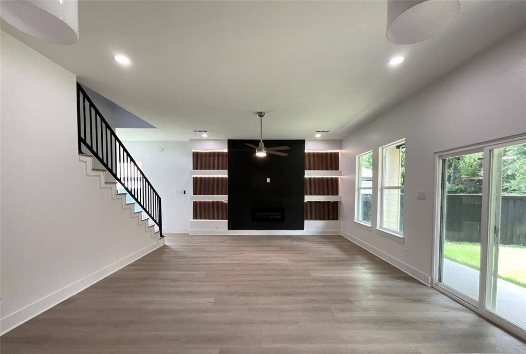 2823 Curvilinear Court, Dallas, TX 75227 Spacious living area featuring wood-finish flooring, a modern black fireplace wall with integrated shelving and accent lighting, and a contemporary black metal staircase railing