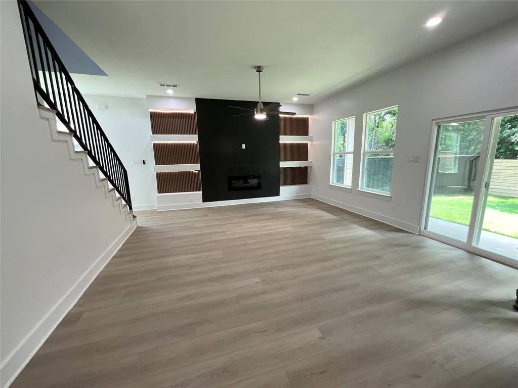 2823 Curvilinear Court, Dallas, TX 75227 Expansive living area featuring light wood-finish flooring, a modern black fireplace surround with an electric fireplace, and integrated shelving with accent lighting
