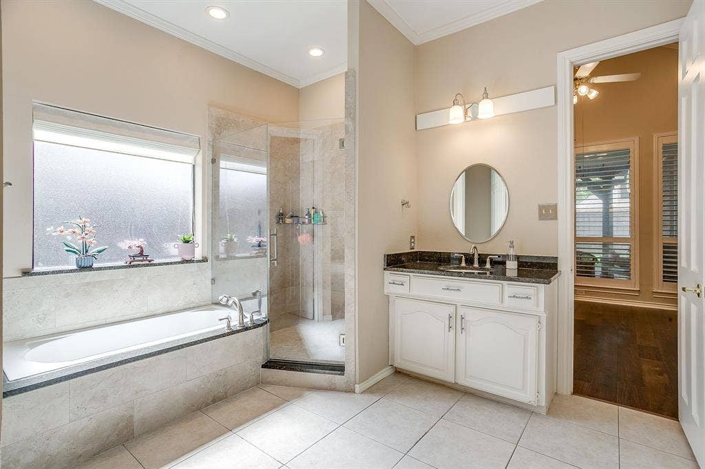 4624 Reunion Drive, Plano, TX 75024 Spacious bathroom featuring a built-in bathtub, a walk-in shower with clear glass enclosure, a vanity with dark countertop and white cabinetry, recessed lighting, and tile flooring