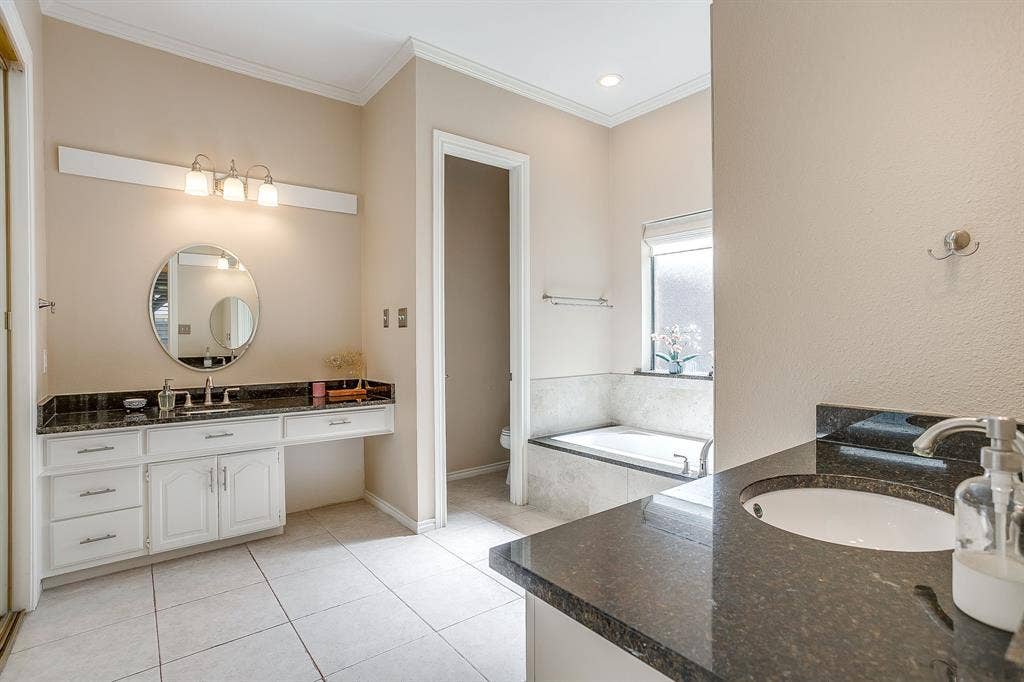 4624 Reunion Drive, Plano, TX 75024 Bathroom featuring dual vanity areas with dark granite countertops, white cabinetry, and white tile flooring