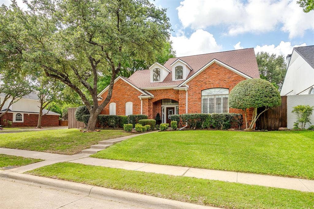 4624 Reunion Drive, Plano, TX 75024 Brick facade residence featuring a front lawn, mature trees, landscaping, and an arched entry