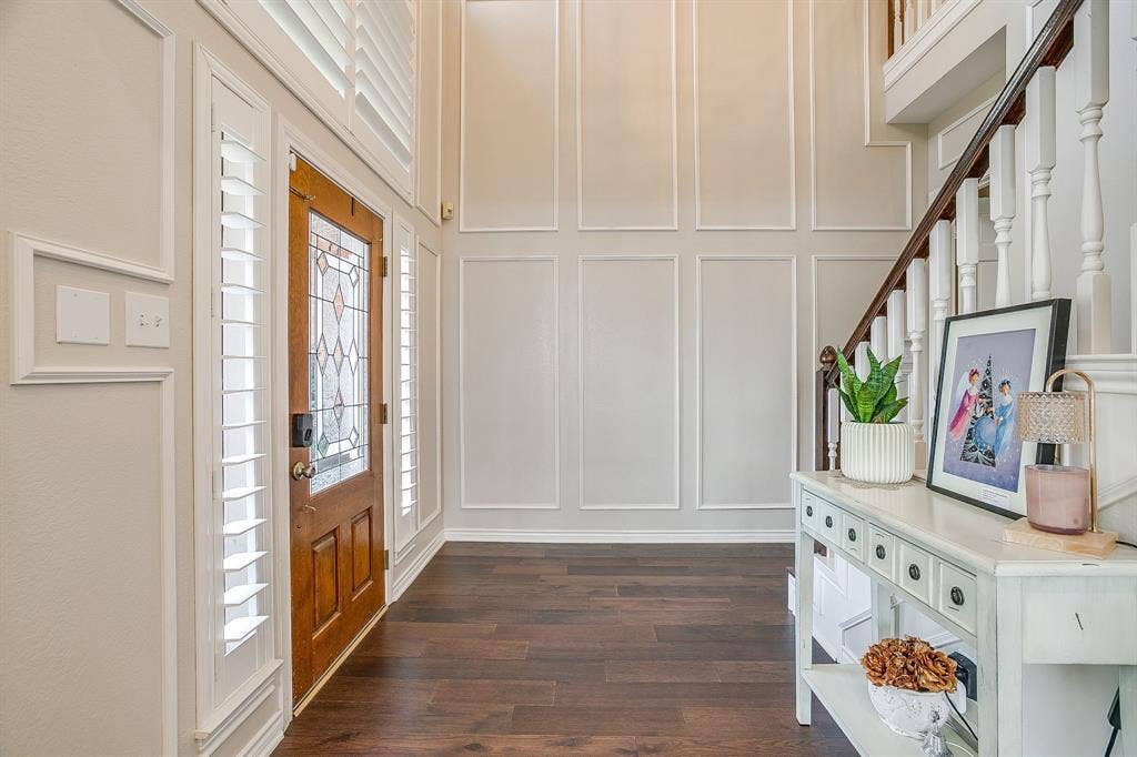 4624 Reunion Drive, Plano, TX 75024 Two-story foyer featuring engineered hardwood flooring, a wood-paneled entry door with leaded glass, white plantation shutters, and extensive wall molding