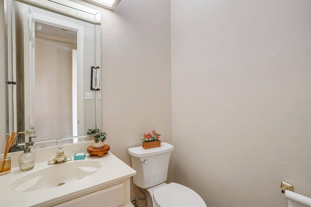 4624 Reunion Drive, Plano, TX 75024 Powder room featuring a white vanity with integrated sink, a beveled mirror, and toilet