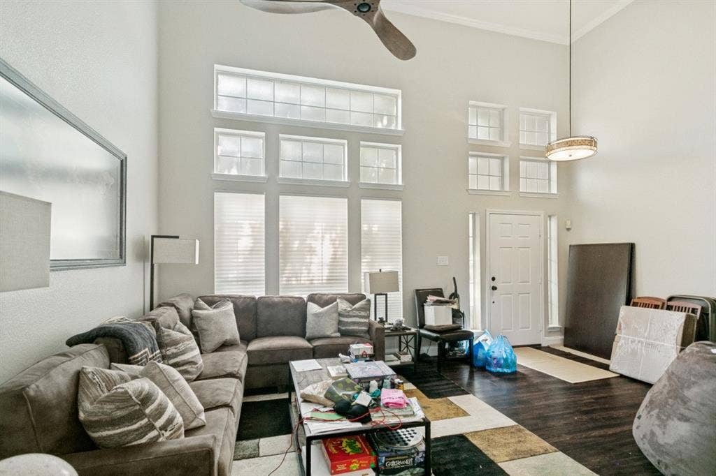 6713 Ashglen Place, Plano, TX 75023 Expansive living space featuring high ceilings, a prominent ceiling fan, dark wood-finish flooring, and multiple large windows with blinds