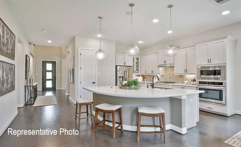 1324 Gardendale Hollow Lane, Anna, TX 75409 Spacious open-concept kitchen featuring a curved island with seating, pendant lighting, white cabinetry, integrated stainless steel appliances, and wood-finish flooring throughout
