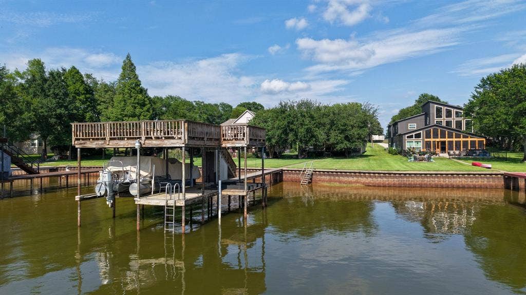 194 Bushwhacker Drive, Mabank, TX 75156 A sweeping view of the waterfront property featuring a park-like lawn, mature trees, and lakeside boathouse.