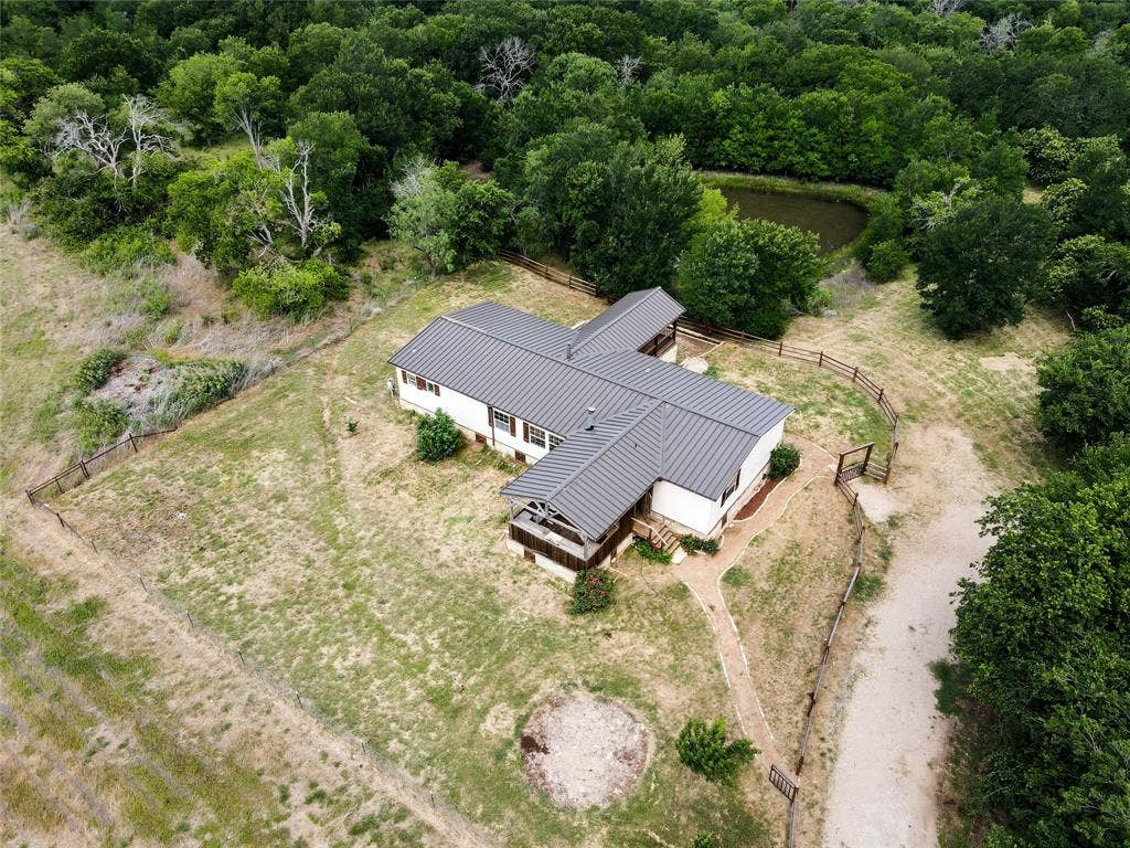 2749 Mcgregor South Loop, McGregor, TX 76657 Aerial property perspective featuring a white-sided residence with a gray metal roof, surrounded by mature trees