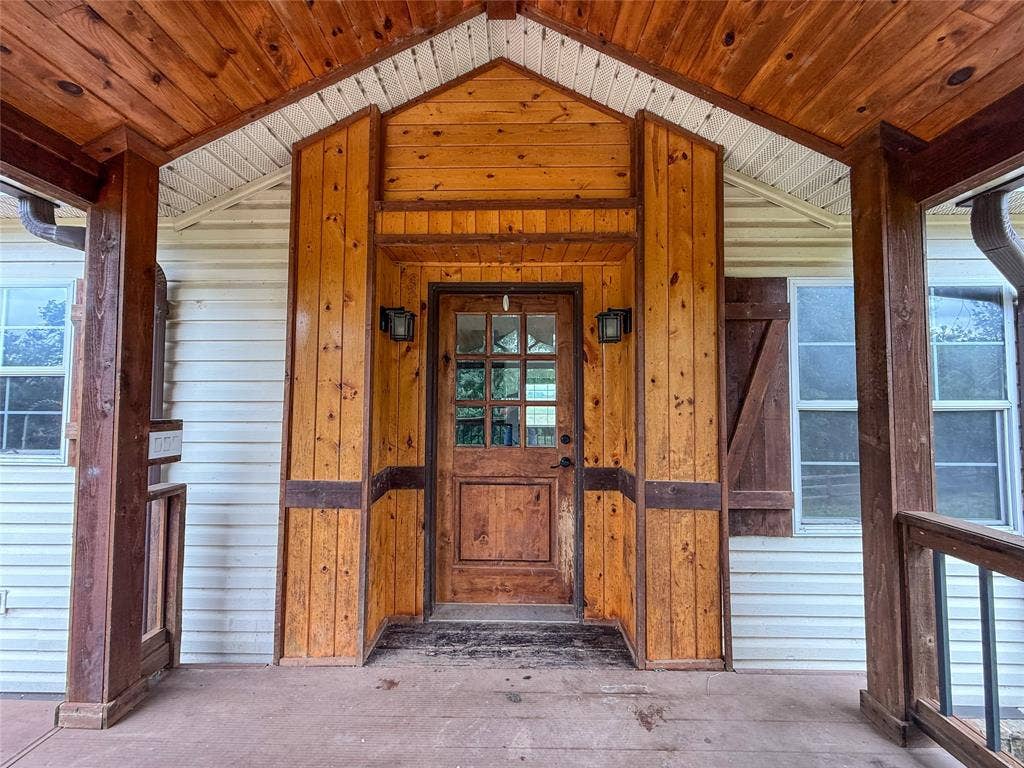 2749 Mcgregor South Loop, McGregor, TX 76657 Inviting front porch featuring a wood-panel accent wall, wood-finish ceiling, and matching wood-paneled entry door with glass inserts