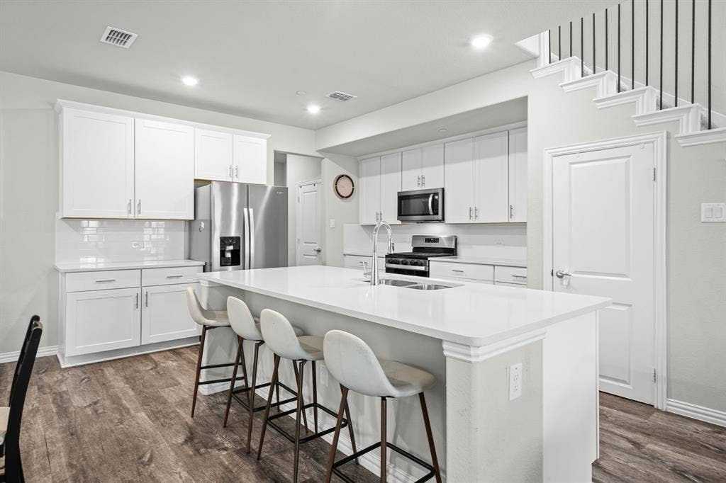 4129 Bullwhip Creek Lane, Sachse, TX 75048 Bright kitchen featuring a substantial island with seating, white shaker cabinetry, stainless steel appliances, white subway tile backsplash, and wood-finish flooring