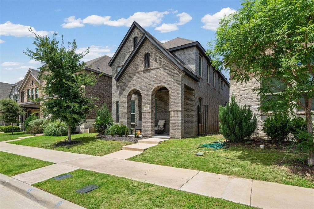 4129 Bullwhip Creek Lane, Sachse, TX 75048 Traditional-style residence featuring a gray brick exterior, arched entryway, and a prominent peaked roofline