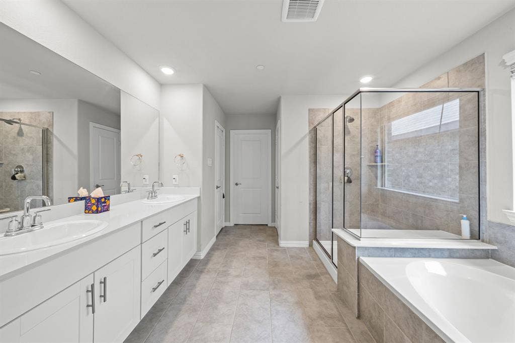 4129 Bullwhip Creek Lane, Sachse, TX 75048 Spacious bathroom featuring a dual vanity with white cabinetry, a large frameless mirror, a glass-enclosed shower, a built-in tub, and tile flooring