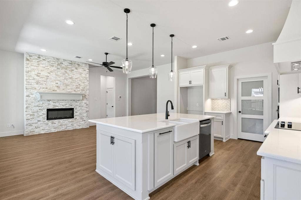 902 Boston Lane, River Oaks, TX 76114 Open-concept living space featuring a central island with a farmhouse sink, white cabinetry, integrated cooktop, and an accent fireplace with a mantel