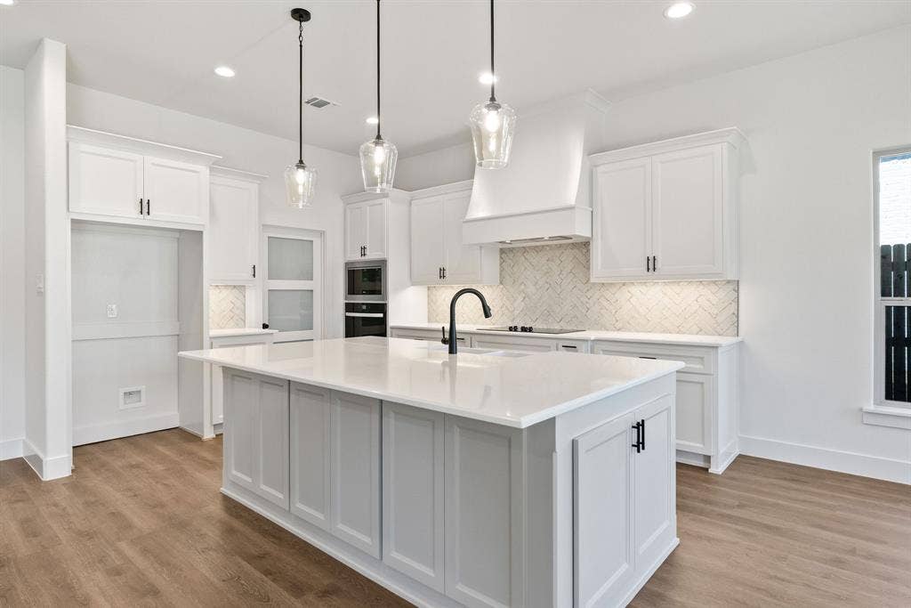 902 Boston Lane, River Oaks, TX 76114 Kitchen featuring a central island with a solid surface countertop, white cabinetry with matte black hardware, integrated double ovens, and wood-finish flooring