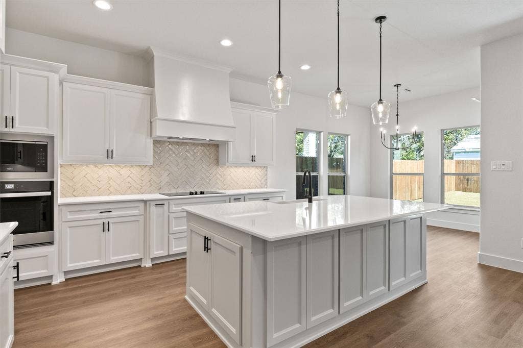 902 Boston Lane, River Oaks, TX 76114 Modern kitchen featuring white shaker cabinetry, an expansive central island with a quartz countertop, stainless steel appliances, a herringbone tile backsplash, and wood-finish flooring