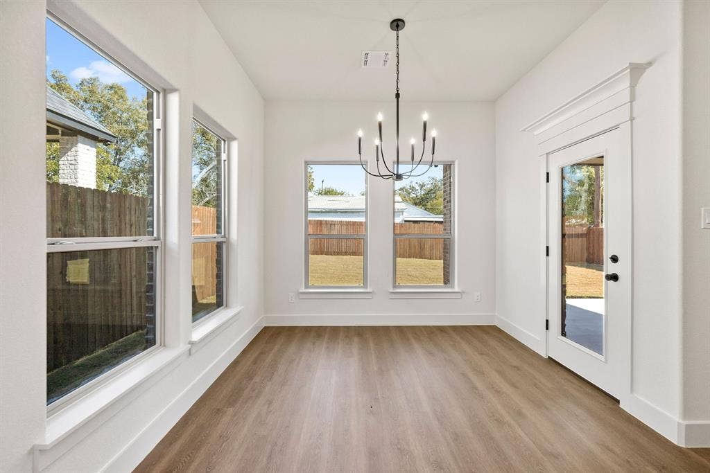 902 Boston Lane, River Oaks, TX 76114 Bright interior space featuring wood-finish flooring, multiple windows, a ceiling-mounted chandelier, and a glass-paned door with decorative trim