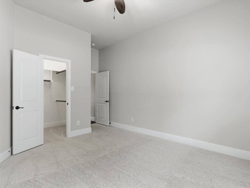 1621 Lakemere Drive, Prosper, TX 75078 Carpeted room featuring a ceiling fan, light gray wall paint, white baseboards, and a walk-in closet with shelving and hanging rods