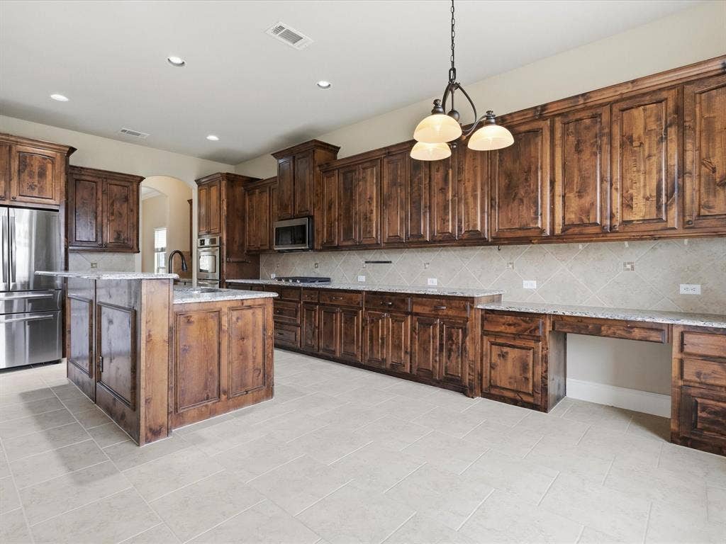 1621 Lakemere Drive, Prosper, TX 75078 Expansive kitchen featuring wood cabinetry, granite countertops, stainless steel appliances, a center island with breakfast bar, and tile flooring