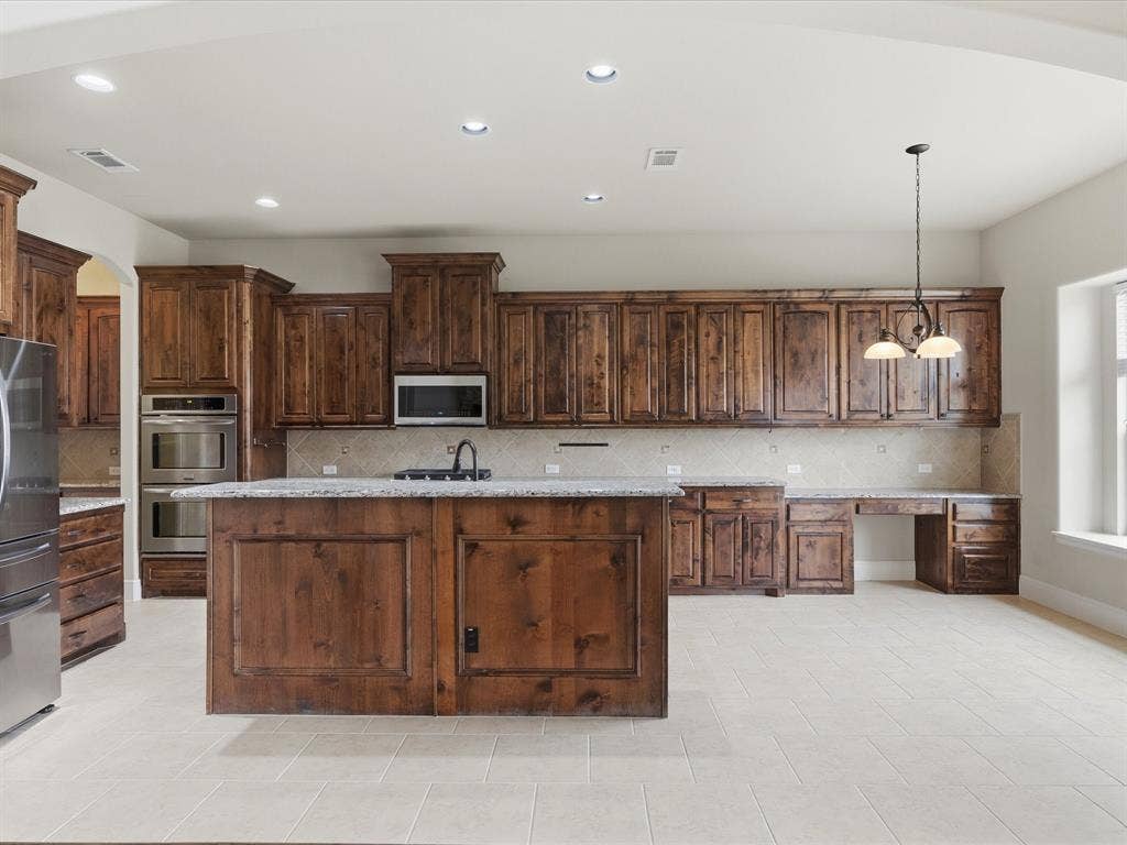 1621 Lakemere Drive, Prosper, TX 75078 Kitchen featuring a central island, wood-finish cabinetry, stainless steel appliances, and light tile flooring