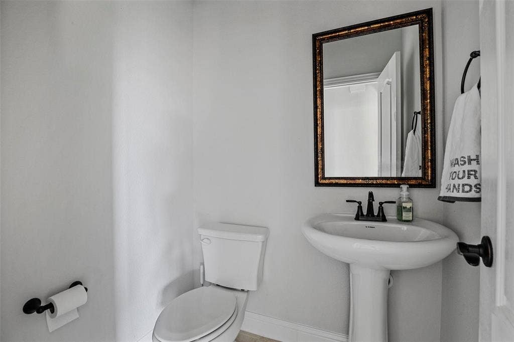 508 Bush Avenue, Waxahachie, TX 75165 Pedestal sink with dark-toned fixtures, rectangular mirror with an ornate frame, and light-toned wall finishes