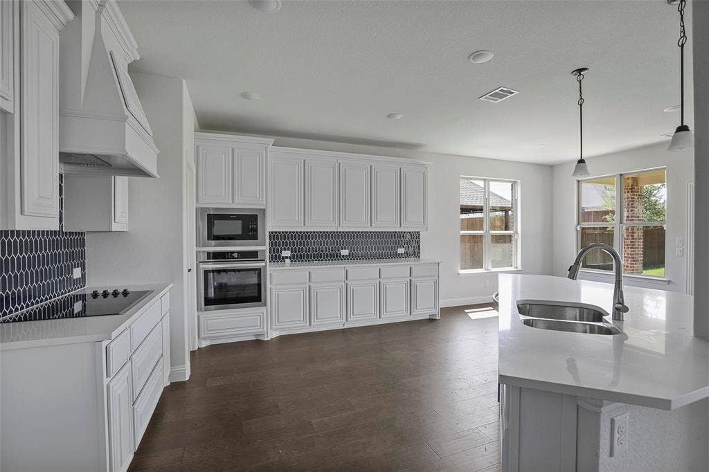 508 Bush Avenue, Waxahachie, TX 75165 Contemporary kitchen featuring an island with a double basin sink, white cabinetry, integrated stainless steel appliances, and wood-finish flooring