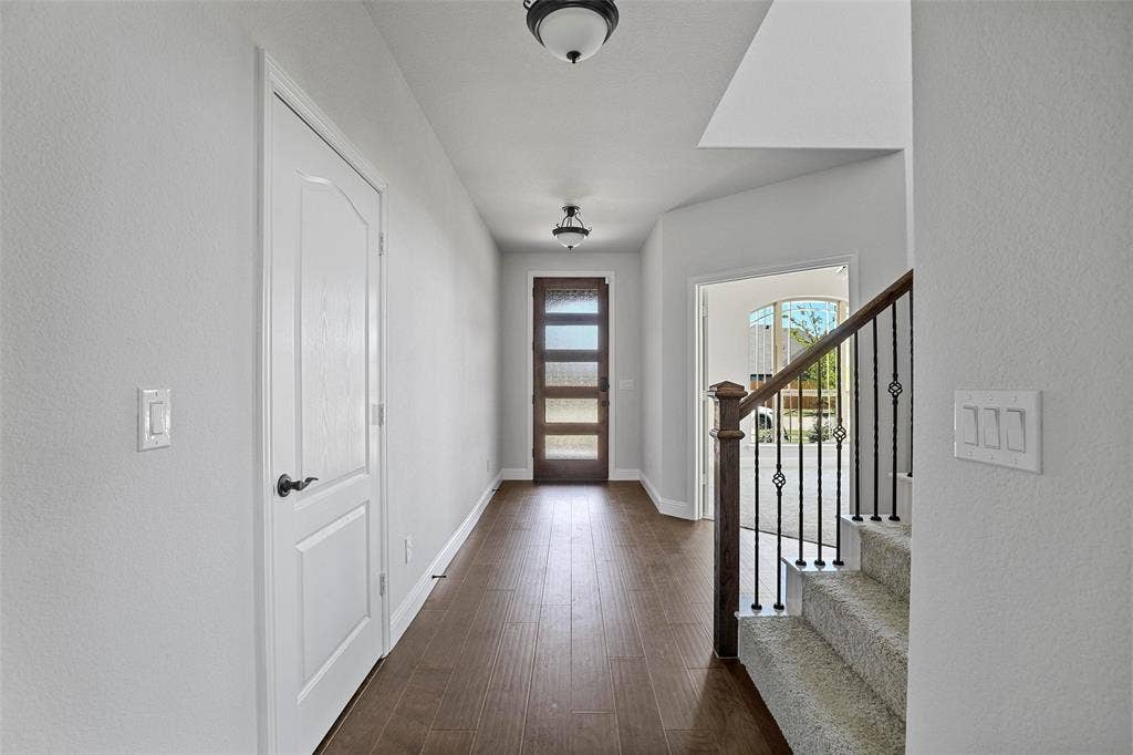 508 Bush Avenue, Waxahachie, TX 75165 Entryway featuring wood-finish flooring, a contemporary front door with frosted glass panels, and a carpeted staircase with wrought iron balusters and a dark wood handrail