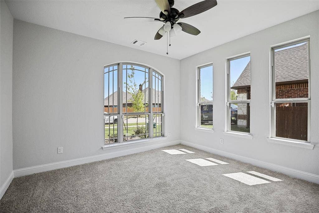 508 Bush Avenue, Waxahachie, TX 75165 Room featuring light-toned walls, gray carpeting, a multi-pane arched window, three vertical windows, and a ceiling fan with integrated lighting