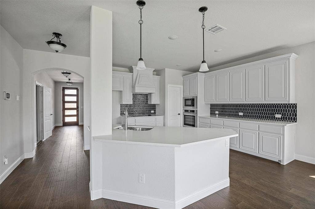 508 Bush Avenue, Waxahachie, TX 75165 Modern kitchen featuring an expansive center island with a white countertop, white cabinetry, a black geometric tile backsplash, and dark wood-finish flooring