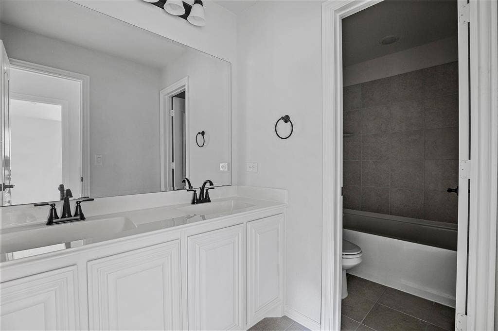 508 Bush Avenue, Waxahachie, TX 75165 Dual vanity with white cabinetry and integrated sinks, featuring black-finished faucets and a large wall-mounted mirror