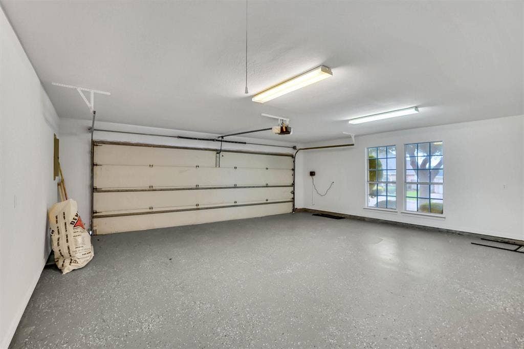 428 Shelby Drive, Burleson, TX 76028 Spacious garage featuring a durable speckled epoxy floor, white painted walls, and ample overhead fluorescent lighting