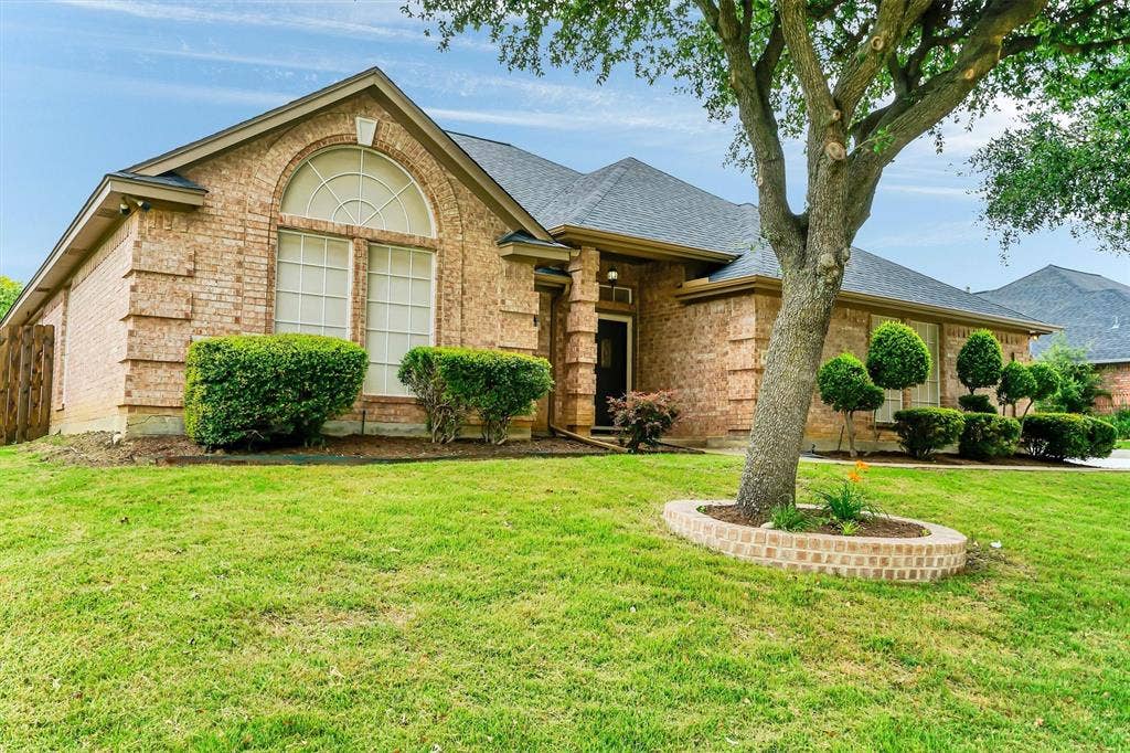 428 Shelby Drive, Burleson, TX 76028 Traditional brick exterior with an arched transom window, a dark-toned entry door, a low-pitched roofline, and established front landscaping