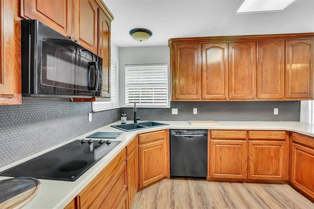 428 Shelby Drive, Burleson, TX 76028 Kitchen featuring warm wood cabinetry, light countertops, a built-in cooktop, and a black double-basin sink with a matte black faucet