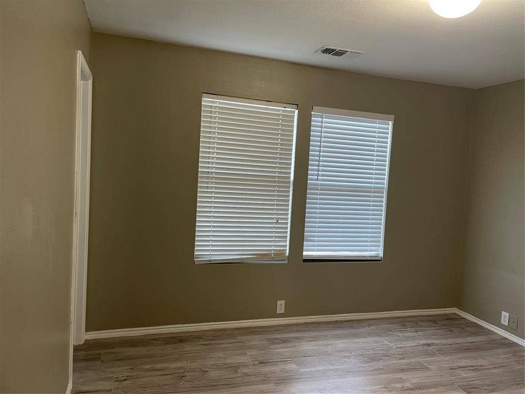 817 Greene Way, Wylie, TX 75098 Interior space featuring wood-finish flooring, two windows with blinds, a white ceiling light fixture, and neutral painted walls