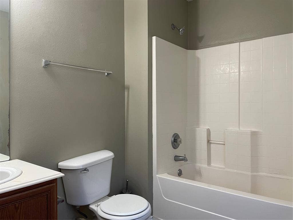 817 Greene Way, Wylie, TX 75098 Bathroom featuring a white bathtub and shower surround, a white toilet, and a wood-finish vanity with a white countertop and integrated sink