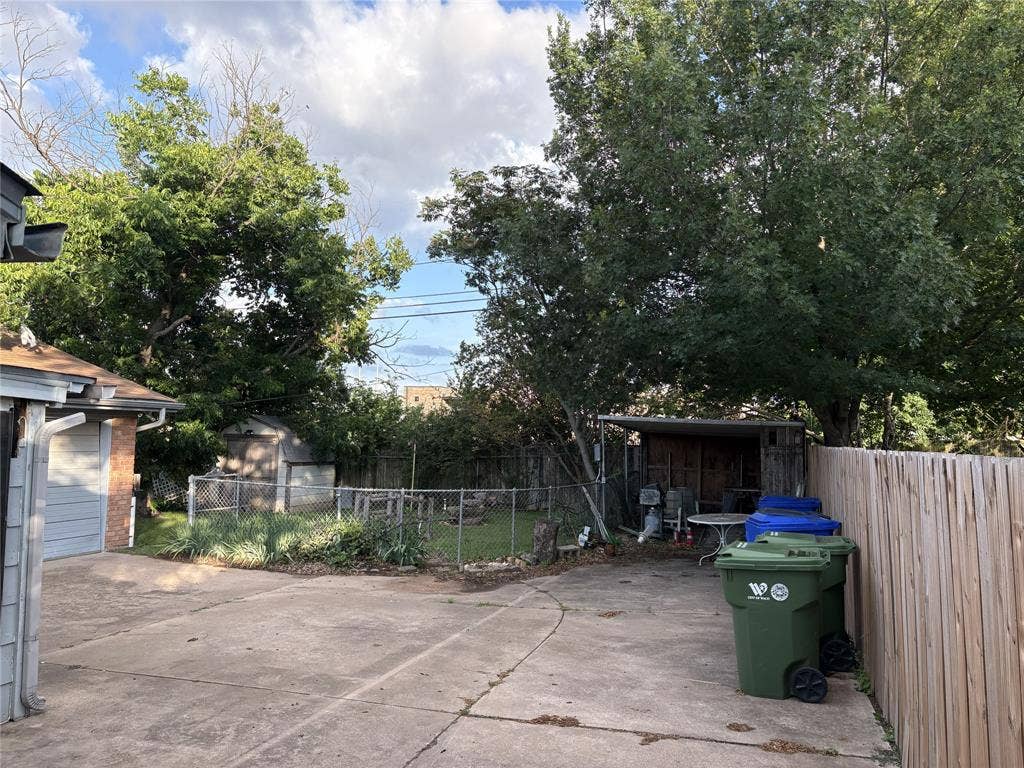 6100 Landmark Drive, Waco, TX 76710 Expansive concrete driveway and patio area featuring a sturdy wooden privacy fence, mature trees, and a chain-link fence enclosing a grassy section