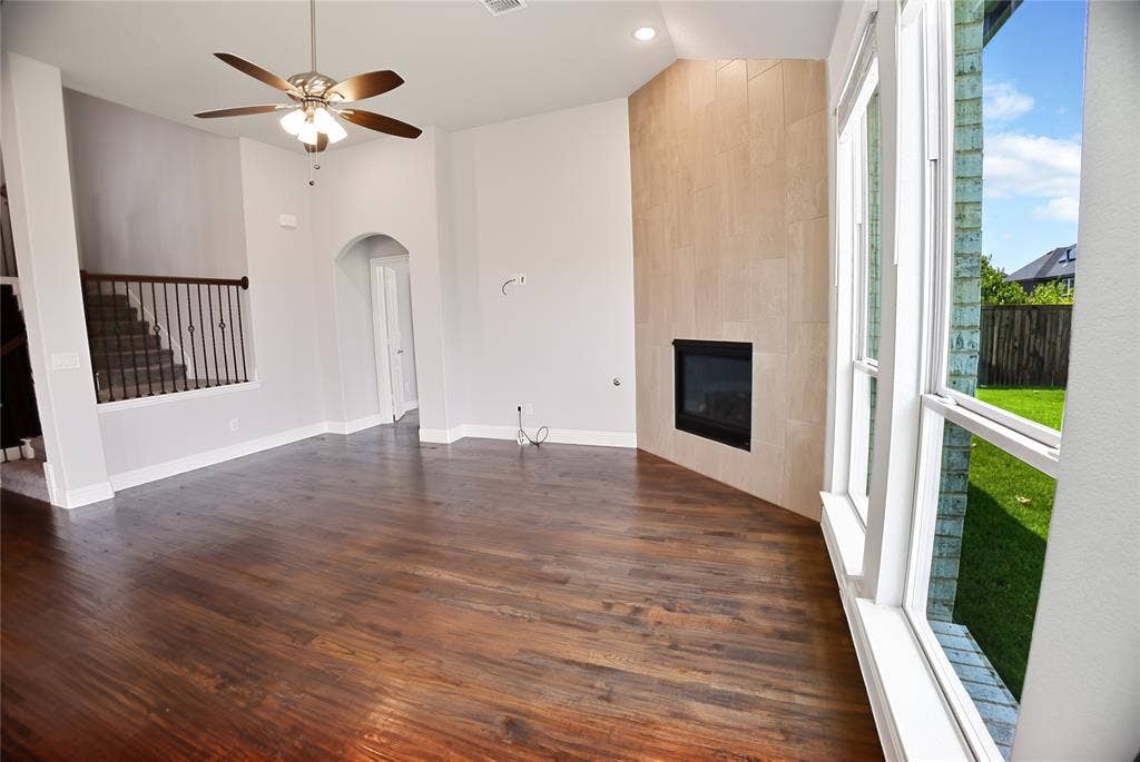 620 Shadow Trail, Frisco, TX 75033 Spacious living area featuring rich wood-finish flooring, a contemporary fireplace with a light-toned tile surround, and multiple large windows