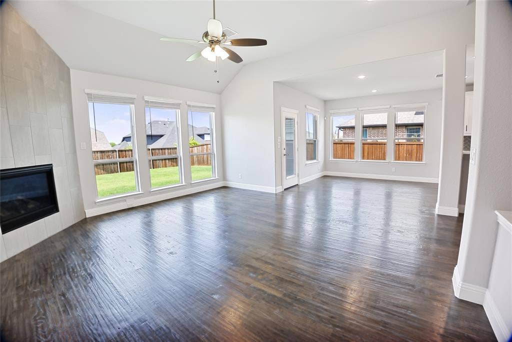 620 Shadow Trail, Frisco, TX 75033 Spacious living area featuring dark wood-finish flooring, a contemporary fireplace with a light-toned tile surround, and an angled vaulted ceiling with a ceiling fan