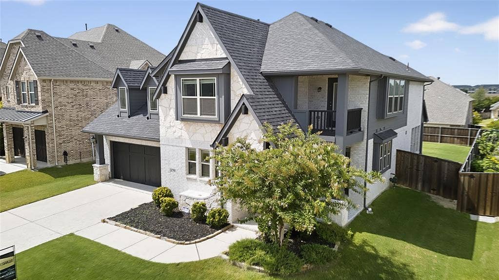 620 Shadow Trail, Frisco, TX 75033 Contemporary two-story exterior featuring white stone and grey siding accents, a dark shingle roof, an attached two-car garage with a dark panel door, and a private second-story balcony