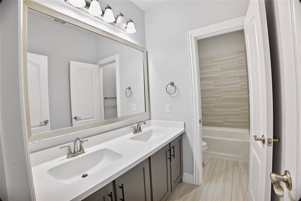 620 Shadow Trail, Frisco, TX 75033 Dual vanity with integrated sinks, brushed nickel fixtures, a large framed mirror, and a five-light vanity bar