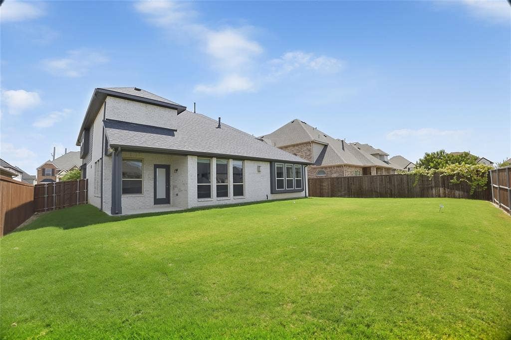 620 Shadow Trail, Frisco, TX 75033 Spacious backyard featuring a manicured lawn, full privacy fencing, and a white brick exterior with dark trim