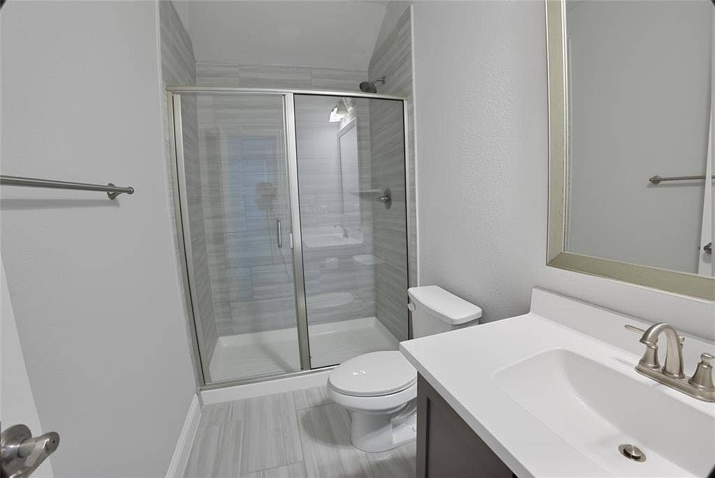 620 Shadow Trail, Frisco, TX 75033 Bathroom featuring a glass-enclosed shower with tile surround, a single vanity with a white countertop and undermount sink, brushed nickel faucet, and a framed mirror